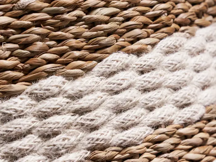 Nærbillede af en vævet overflade med skiftevis tykt, snoet lysbeige reb og naturbrunt reb, der skaber et struktureret, stribet mønster.