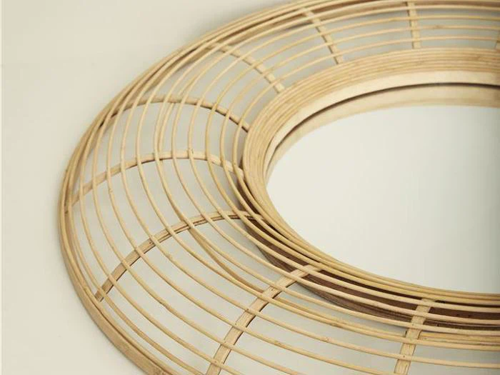 Nærbillede af et rundt spejl med en dekorativ ramme lavet af tynde, jævnt fordelte træ- eller bambusstrimler, der danner et geometrisk, cirkulært mønster.