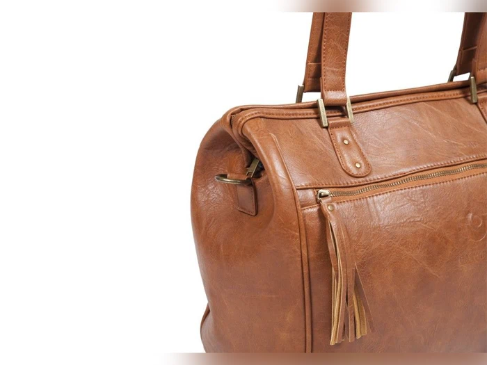 Et nærbillede af en brun læderhåndtaske med lynlåslomme foran, kvastdetaljer og robuste håndtag på en almindelig hvid baggrund.