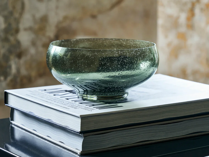 En gennemsigtig grøn glasskål står oven på to stablede indbundne bøger med hvide omslag på en mørk bordplade.