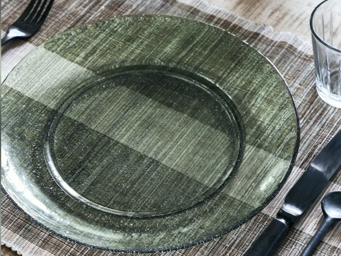 En klar glastallerken på en vævet dækkeserviet med en gaffel, kniv, ske og et tomt drikkeglas ved siden af.