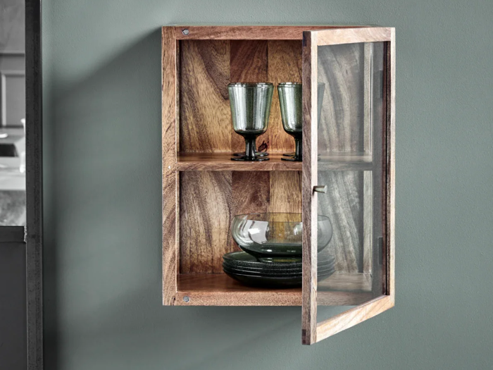 Et lille væghængt træskab med glasdør, der indeholder to grønne glas på den øverste hylde og grønne skåle og tallerkener på den nederste hylde.