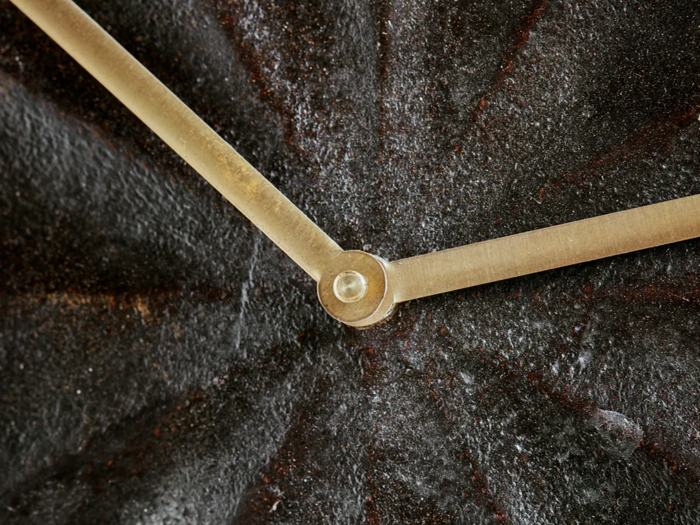 Nærbillede af to metalliske urvisere på en struktureret, mørk urskive, der konvergerer i midten, hvor de er forbundet med en lille cirkulær lukning.