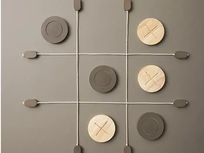 Tic-tac-toe-spil på en væg med et gitter lavet af reb; store X- og O-brikker af træ placeret på brættet.