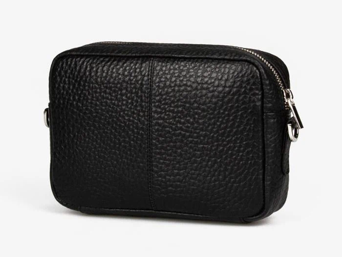 En lille crossbody-taske i sort tekstureret læder med sølvfarvet lynlås og hardware, vist på en almindelig hvid baggrund.