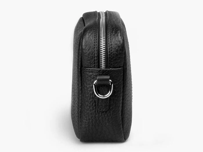 Sidebillede af en sort tekstureret lædertaske med synlig lynlås og en D-ring i metal for enden på en almindelig hvid baggrund.