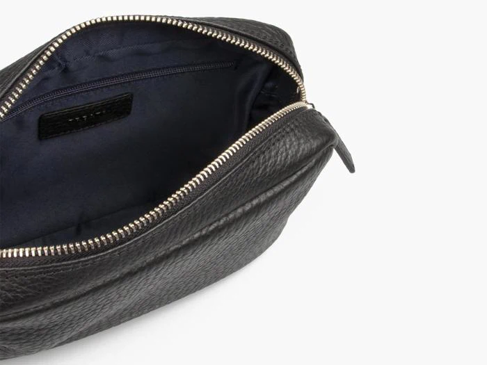 Et nærbillede af en åben sort læderpung med guldlynlås, der viser et mørkt stofinteriør og en indvendig lynlåslomme.