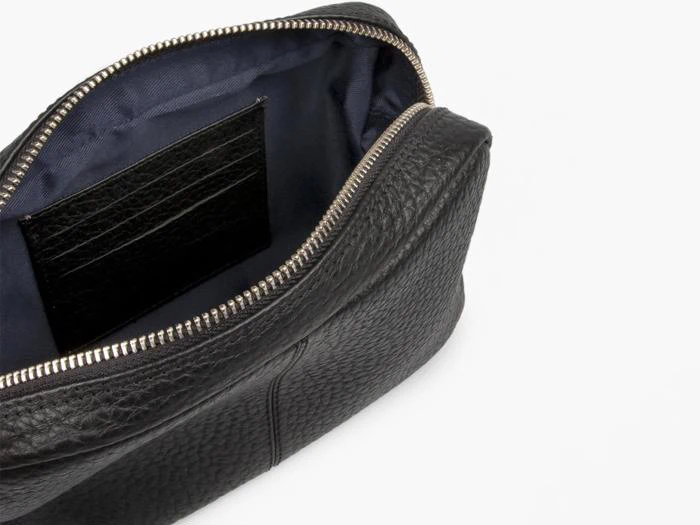 Et nærbillede af en åben sort lædertaske med sølvlynlås, der viser et mørkt stofinteriør og en inderlomme.