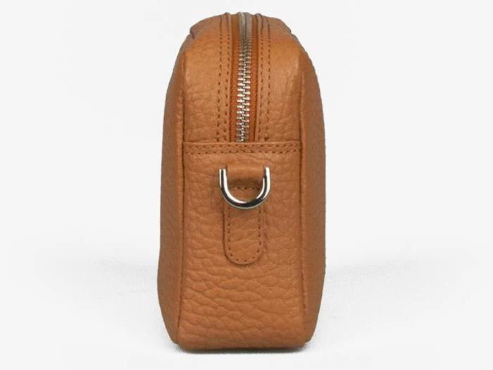 Sidebillede af en brun læderpung med en sølvfarvet D-ring i metal og en synlig lynlås på toppen, placeret mod en almindelig hvid baggrund.