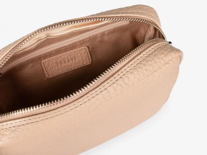 En beige tekstureret lynlåspose er åben og viser sit glatte brune stoffor og en rektangulær etiket, der er syet på indersiden.