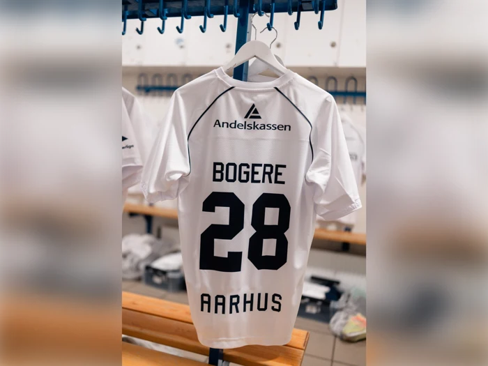 En hvid fodboldtrøje med navnet BOGERE, nummeret 28 og AARHUS trykt på ryggen, der hænger i et omklædningsrum.