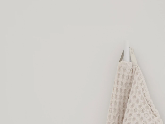 Et beigefarvet håndklæde med struktur hænger på en hvid krog mod en almindelig hvid væg.