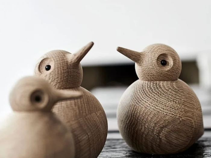 Tre fuglefigurer af træ med runde kroppe og spidse næb er placeret tæt sammen på en flade med en sløret baggrund.
