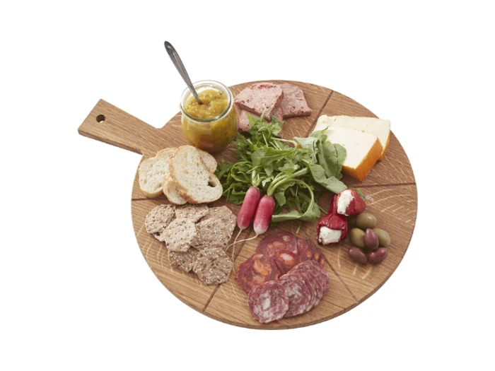 Rundt serveringsbræt i træ med forskellige oste, kødpålæg, kiks, brødskiver, radiser, oliven, rucola og et glas chutney med en ske.