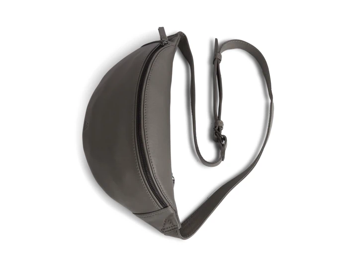 Grå crossbody-taske i læder med en buet halvmåneform, synlig lynlåslukning og en justerbar rem, der er arrangeret i en løs hjerteform.