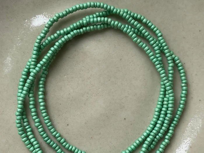 Flere tråde af små, runde, mintgrønne perler er viklet på en lys beige overflade.