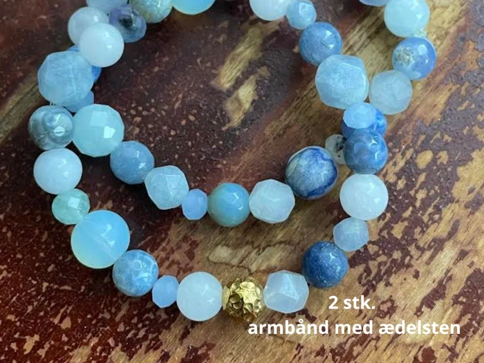 To perlearmbånd af ædelsten i blå og hvide toner på en træoverflade. Tekst: 2 stk. armbånd med ædelsten.