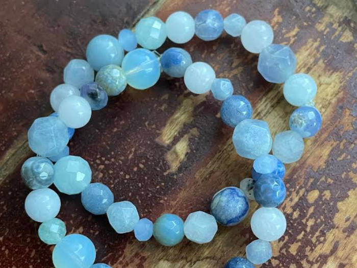 To perlearmbånd af runde og facetterede blå og hvide sten hviler på en træoverflade.