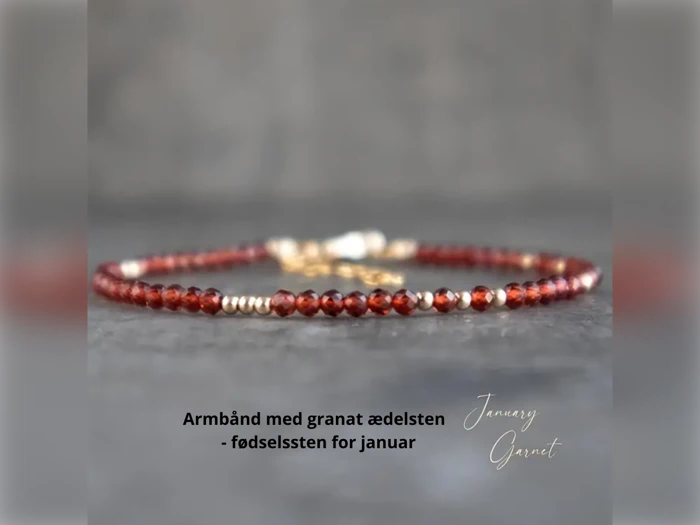 Et delikat armbånd med små, facetterede granatædelsten og guldaccenter på en grå overflade. Dansk tekst: Armbånd med granat ædelsten - fødselssten for januar.