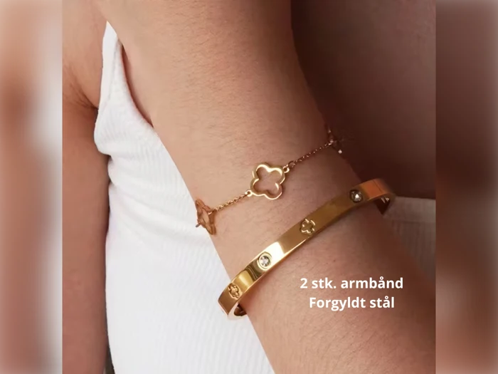 En person bærer to guldfarvede armbånd, et fint med en blomstercharm og et massivt med indlejrede sten. Teksten lyder: 2 stk. armbånd Forgyldt stål.