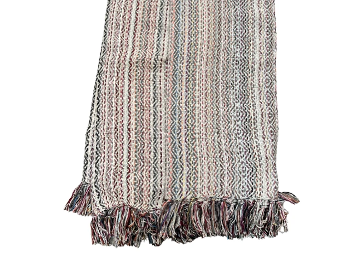 Et flerfarvet vævet tæppe med lodrette striber og frynsede kanter, med en blanding af sorte, røde og hvide tråde i et geometrisk mønster.