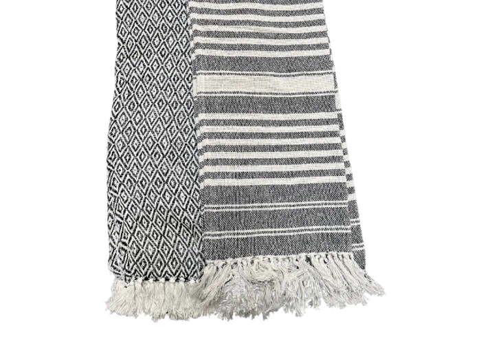 Et foldet sort-hvidt vævet tæppe med et diamantmønster på den ene side og striber på den anden side, som begge ender i frynser.