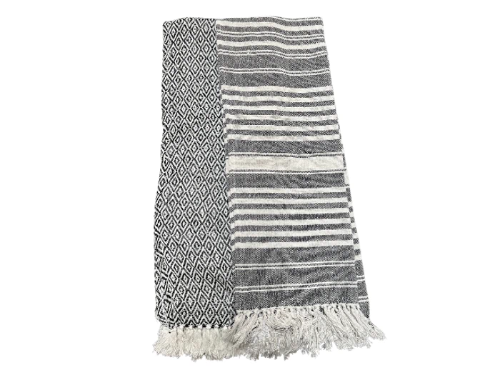 Foldet sort-hvidt tæppe med frynser, med geometriske diamantmønstre på den ene side og vandrette striber på den anden side.