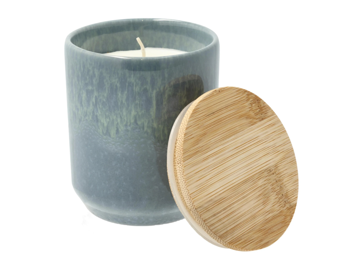 En grå keramikkrukke med et hvidt vokslys indeni, vist ved siden af et rundt bambuslåg, der hviler i en vinkel.