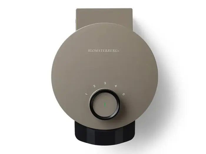 Et topbillede af et rundt, taupefarvet Blomsterbergs vaffeljern med en nummereret skive i midten.