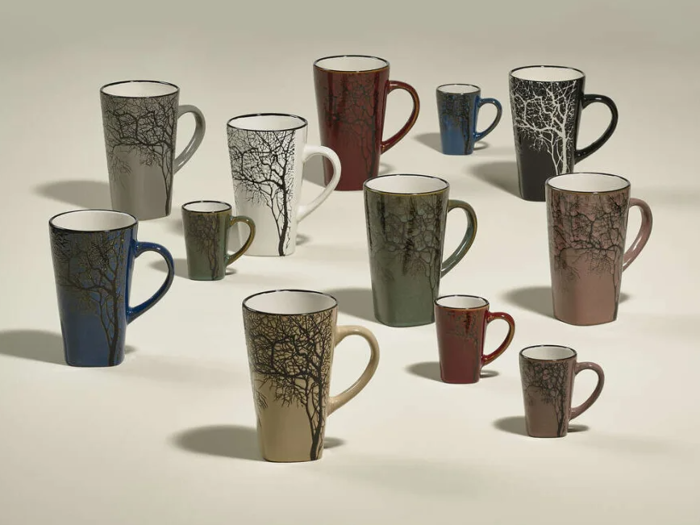 En gruppe keramikkrus i forskellige farver og størrelser, hver dekoreret med et sort grenmønster, anbragt på en lys overflade.
