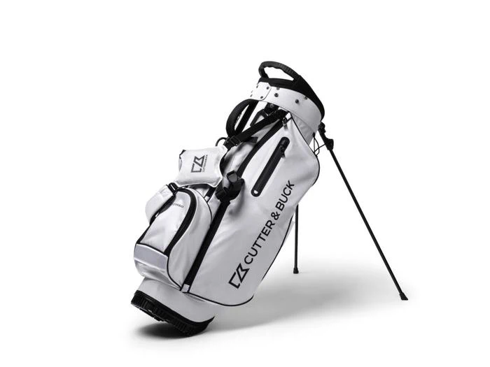 Hvid Cutter & Buck golfbag med flere lommer og et stativ, placeret på sine ben mod en hvid baggrund.