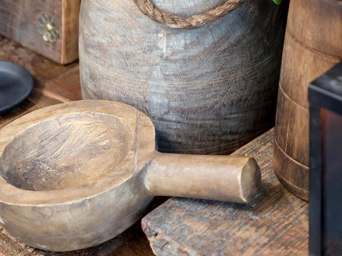 Nærbillede af rustikt køkkenudstyr i træ, bl.a. en rund skål med hank og et stort kar, placeret på en træoverflade.