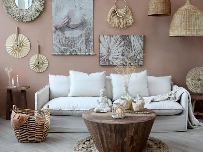 Stue i boho-stil med en hvid sofa, vævet indretning, stearinlys, rattanlamper, et rundt sofabord i træ og neutraltonet vægkunst og tilbehør.