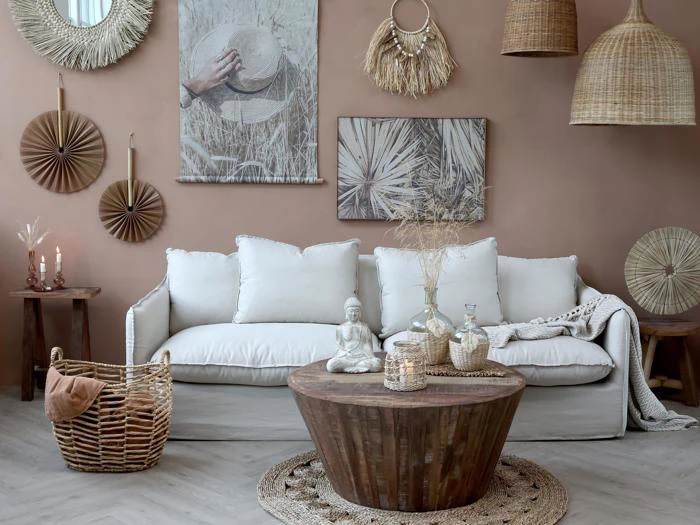 En hyggelig stue med en hvid sofa, et rundt sofabord i træ, flettede kurve, rattanindretning, stearinlys og vægkunst i jordfarver, der skaber en varm boho-atmosfære.