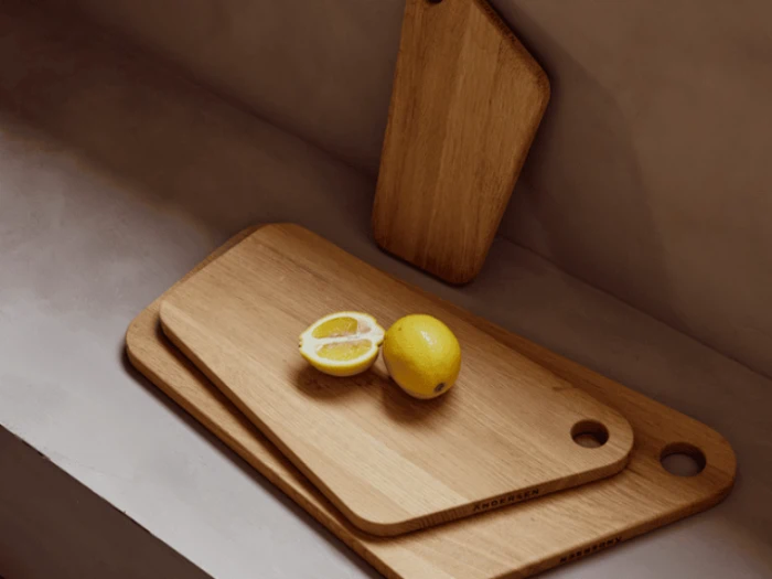 Tre skærebrætter af træ er stablet med en hel og en halv citron placeret ovenpå. Et andet skærebræt læner sig op ad væggen i baggrunden.