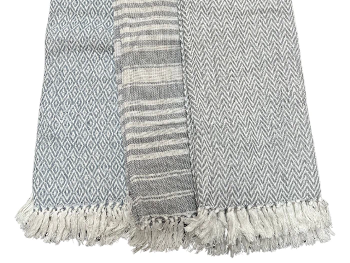 Tre vævede stoffer side om side, hver med et forskelligt gråt og hvidt mønster: diamanter, striber og chevrons, alle med frynsede kanter.