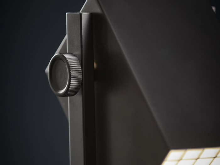 Nærbillede af en sort metalknap på en moderne, geometrisk lampe med et struktureret greb, vist på en mørk baggrund.