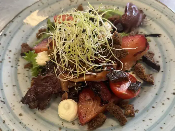 En farverig salat med spirer, cherrytomater, bladgrønt, mørke brødcroutoner og klatter af cremet dressing på en blå plettet tallerken.