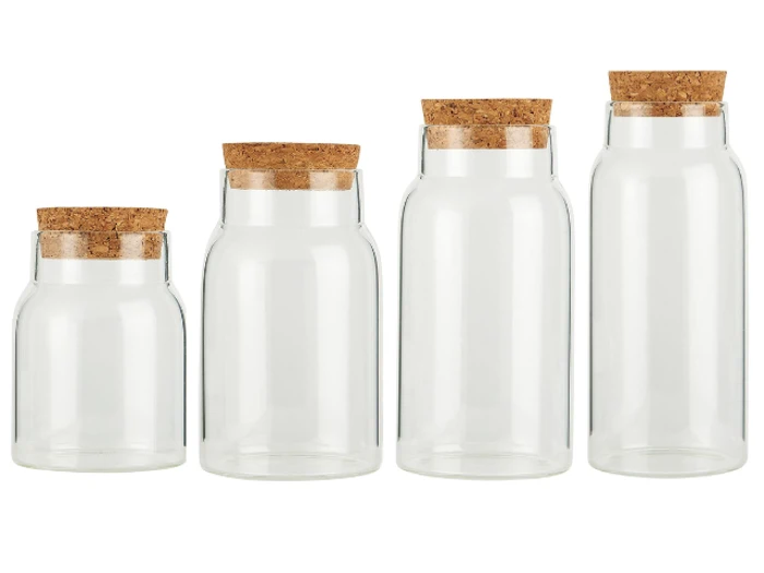 Fire klare glaskrukker i forskellige højder, hver med et korklåg, er arrangeret side om side mod en hvid baggrund.