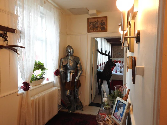 En gang med en rustning, indrammede billeder, potteplanter i vinduet og en dekorativ elgstatue i det tilstødende rum. Væggene er dekoreret med kunst, og lysarmaturerne er tændt.