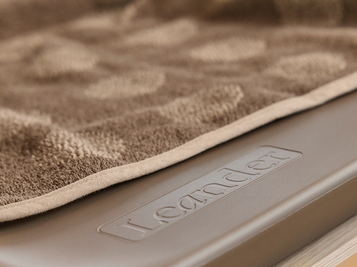 Et nærbillede af et brunt tekstureret håndklæde draperet over en overflade med ordet Leander præget på det.