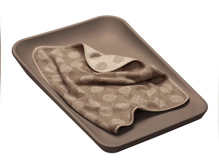 En beige rektangulær bakke med et lysebrunt håndklæde med polkaprikket mønster, delvist foldet, placeret indeni.