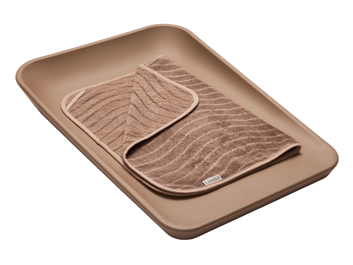 En solbrun rektangulær bakke med et foldet, struktureret brunt håndklæde mærket Tambe placeret indeni.