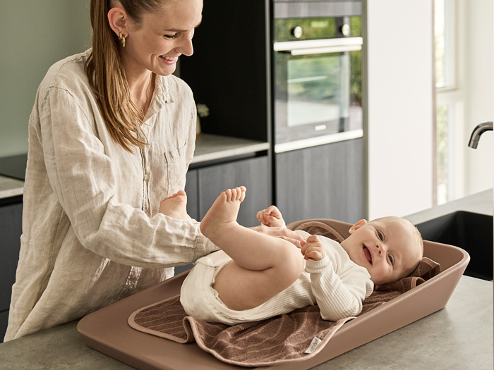 En smilende kvinde skifter ble på en glad baby på en brun puslepude i et moderne køkken.