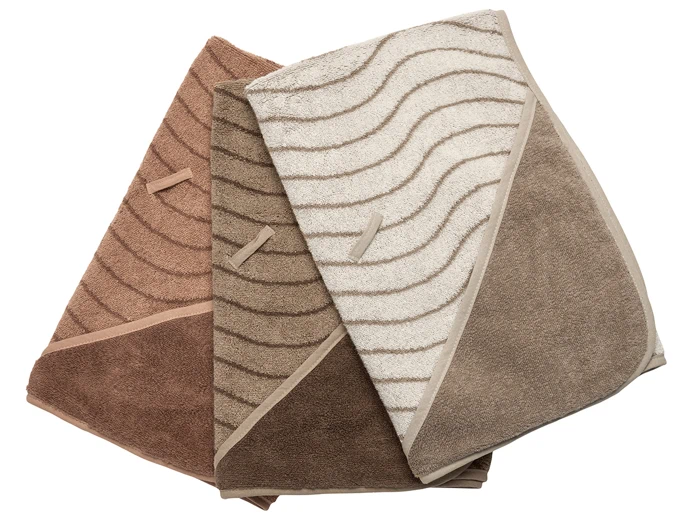 Tre foldede hættehåndklæder i brune, beige og cremefarvede farver med bølgemønstre, lagt side om side på en hvid baggrund.