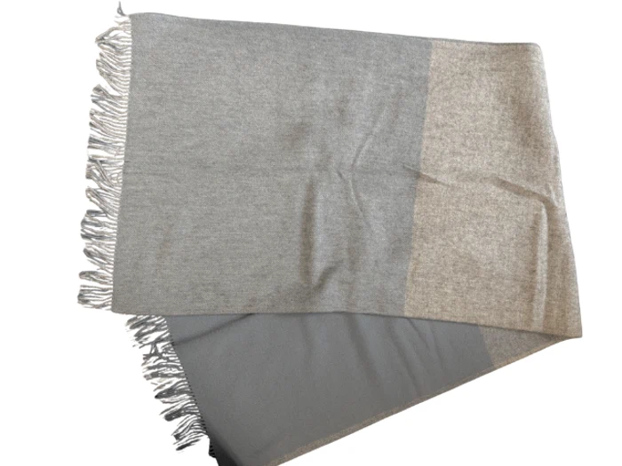 Et tofarvet tørklæde med frynsede kanter, med lysegrå og beige sektioner, lagt fladt på en hvid baggrund.