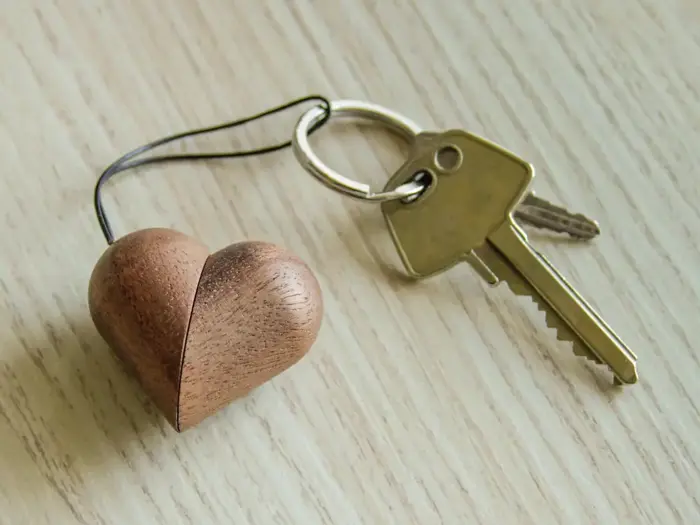 En metalnøglering med to nøgler og en hjerteformet nøglering i træ hviler på en lys træoverflade.