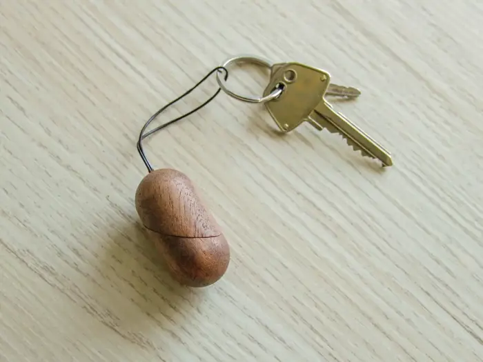 En messingnøgle fastgjort til en nøglering med en lille, brun, oval trænøglering, der ligger på en lys træoverflade.