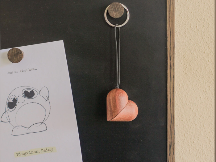 En hjerteformet nøglering af træ hænger på en krog ved siden af en skitse af en tegneseriepingvin med navnet Pingvinen, Daisy, på en tavle.