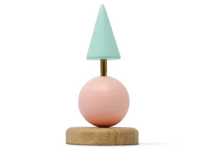 En lille skulptur med en træbase, en pink kugle og en lyseblå kegle på toppen, forbundet med en tynd guldstang.